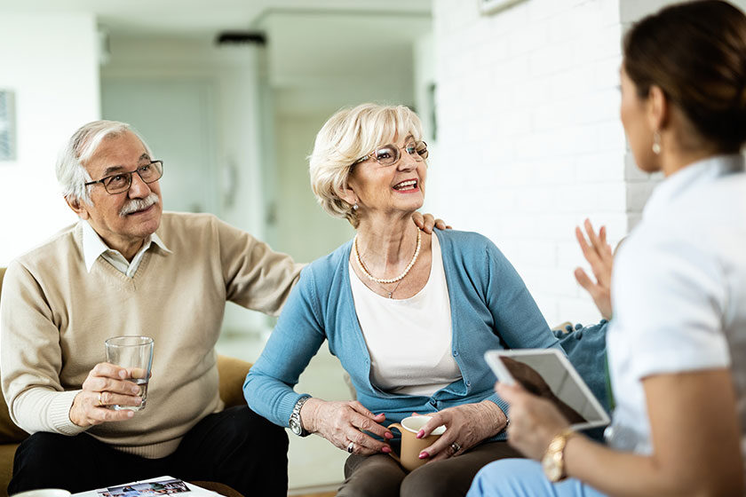 Happy mature couple talking to female nurse who is visiting them at home.