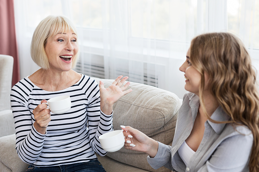 Happy mature mother and daughter drinking coffee and talking